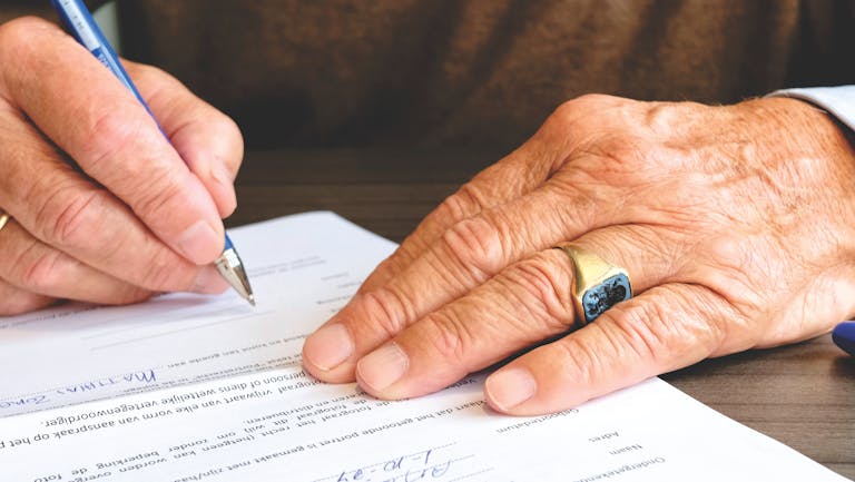 Close-up of a senior adult signing a document meant to represent a Scope of Appointment form.