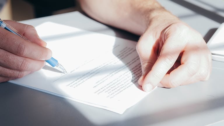 Hands signing a contract with a blue pen, close-up view. Meant to represent signing an ACA Marketplace Consent Form.