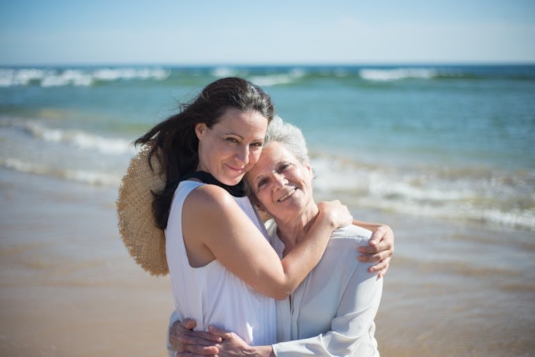 Mother and daughter embrace by ocean.